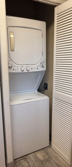 A compact washer and dryer unit with a control panel, located in a small laundry room with a wooden floor.