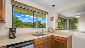 A kitchen with a large window, wooden cabinets, a dishwasher, and a coffee maker. - Hideaways Retreat Villa- North shore princeville (Princeville)