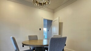 Uma sala de jantar com uma mesa redonda, quatro cadeiras estofadas, um candelabro e soalho em madeira.