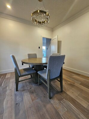 A dining area with a round table, four upholstered chairs, a chandelier, and wooden flooring. - City Retreat (Sugar Land)