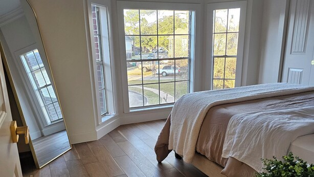 Quarto com cama grande, janela com vista para o exterior e mesa redonda com planta.