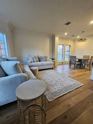 A spacious living room with a large sofa, a round coffee table, and a dining area with a table and chairs. - City Retreat (Sugar Land)