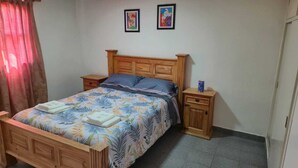 A bedroom with a wooden bed, two nightstands, a small cabinet, and a floral bedspread. - Rio Chico Valley (Gobernador Gregores)