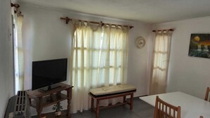 A room with a television on a wooden stand, a small table, a bench, and a painting on the wall. - Rio Chico Valley (Gobernador Gregores)