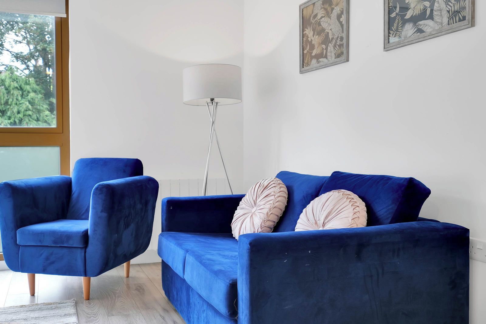 Ein Zimmer mit einem blauen Sofa und zwei passenden Sesseln, einer Stehlampe und zwei gerahmten Bildern an der Wand.