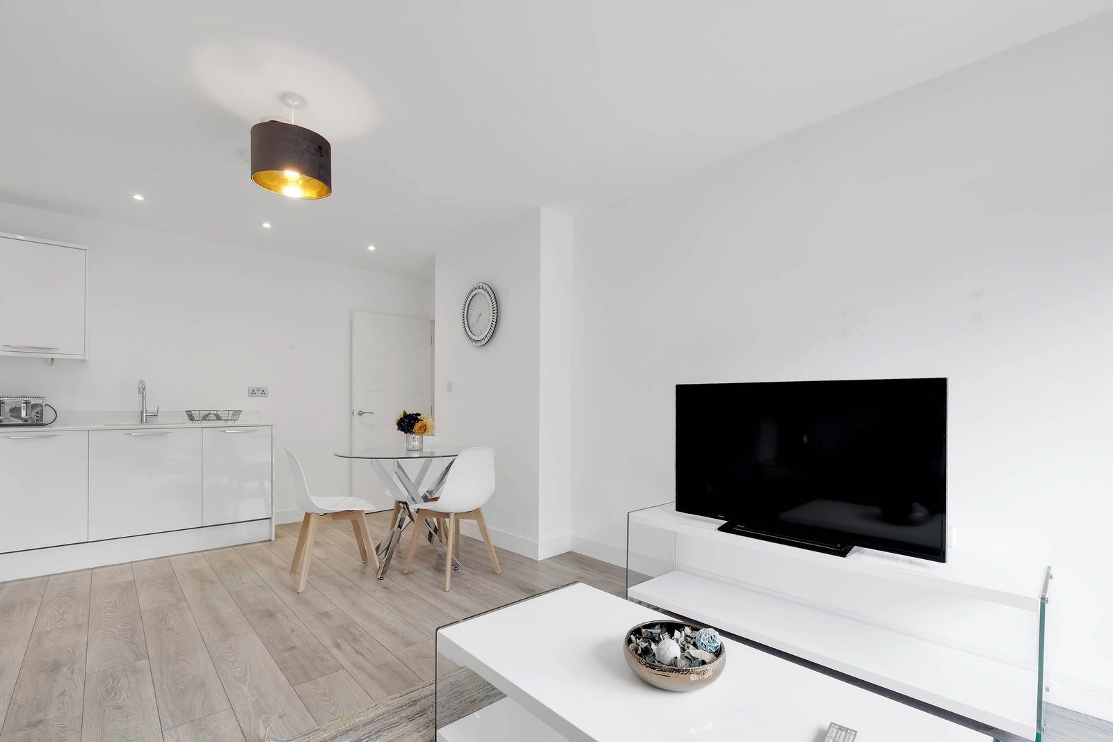 Ein modernes Wohnzimmer mit einem Flachbildfernseher, einem Glastisch und einem Essbereich mit weißem Tisch und Stühlen.