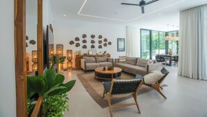 Una sala de estar moderna con sofá, mesa de centro y sillas, un comedor con mesa y sillas, y un amplio ventanal con vista a zonas verdes.