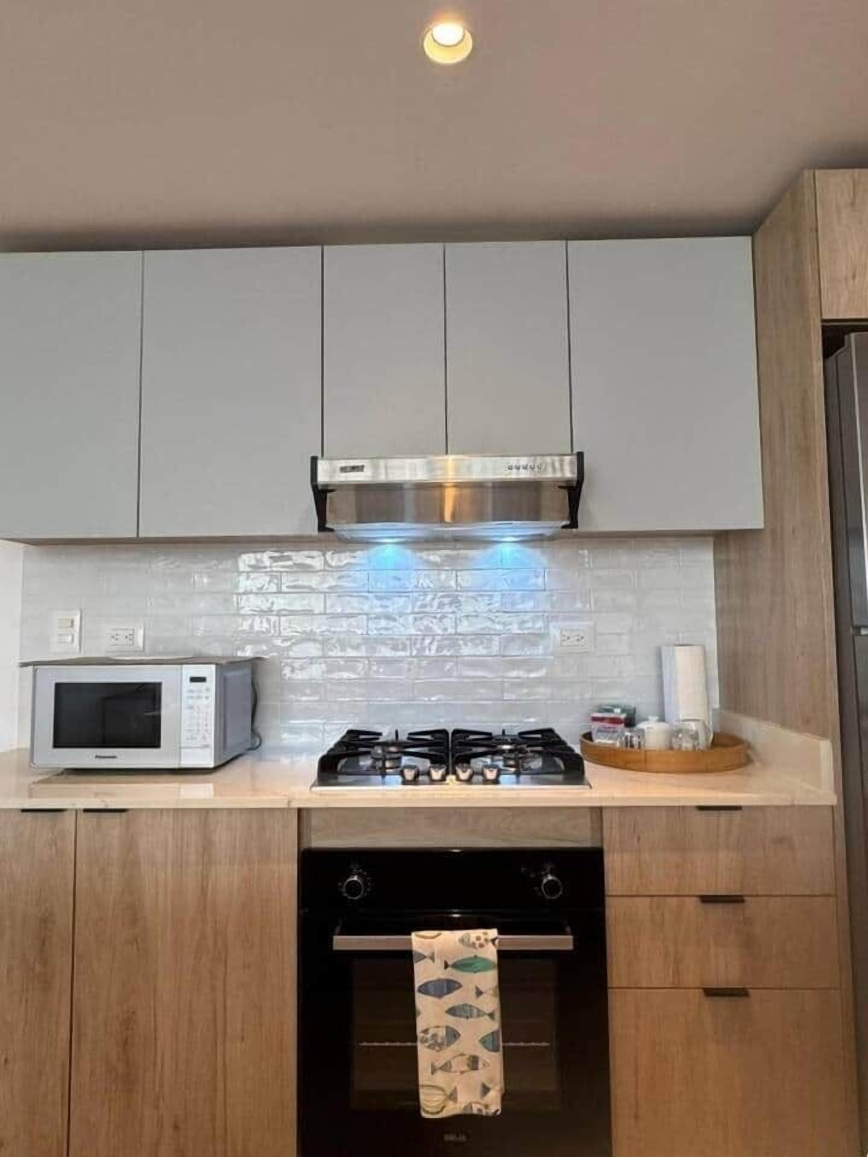 Una cocina con gabinetes grises, una campana extractora de acero inoxidable, un microondas, una estufa a gas y un lavavajillas.
