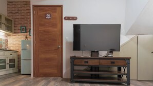 Een kamer met een houten deur, een televisie op een standaard, een kast en een bakstenen muur.