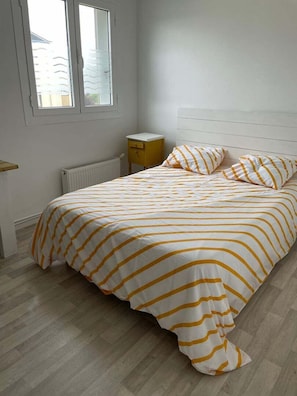 Ein Schlafzimmer mit Bett, Nachttisch, Fenster und Heizkörper.