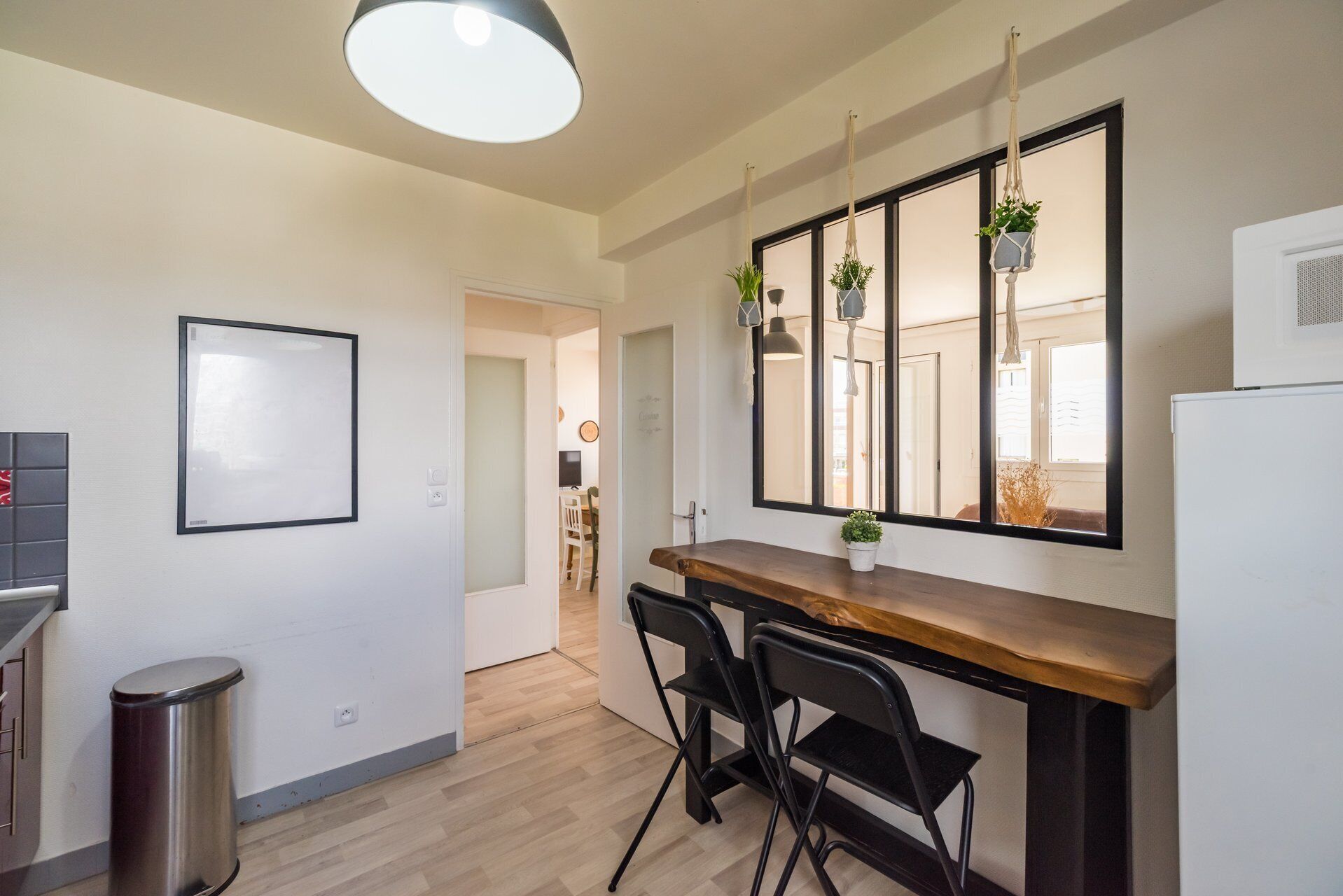 Une cuisine avec un plan de travail en bois, des chaises noires, une plante suspendue et un grand miroir.