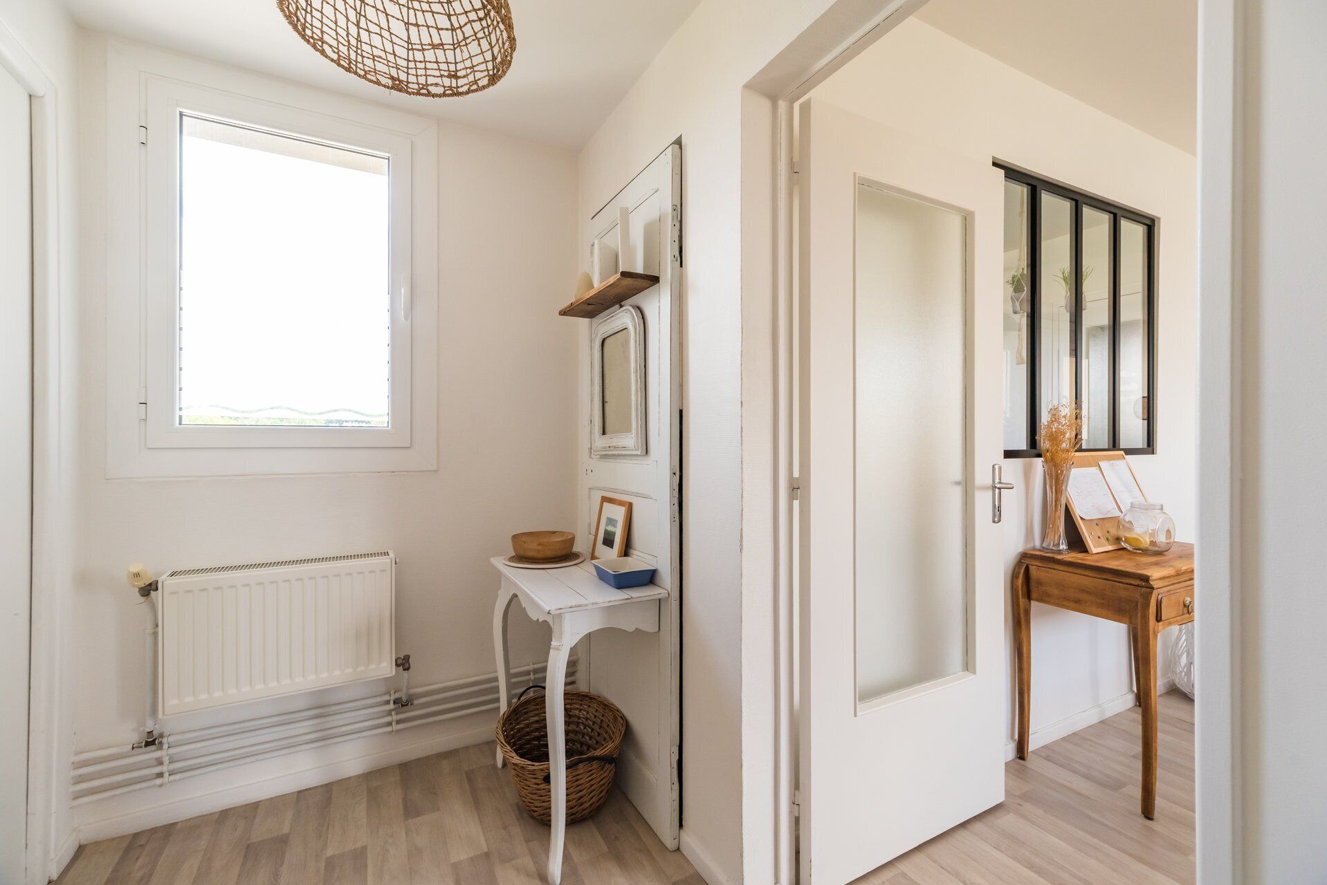 Un couloir avec un radiateur, un panier en osier, une petite table avec un miroir et une porte en bois.