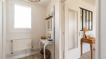 Un couloir avec un radiateur, un panier en osier, une petite table avec un miroir et une porte en bois.
