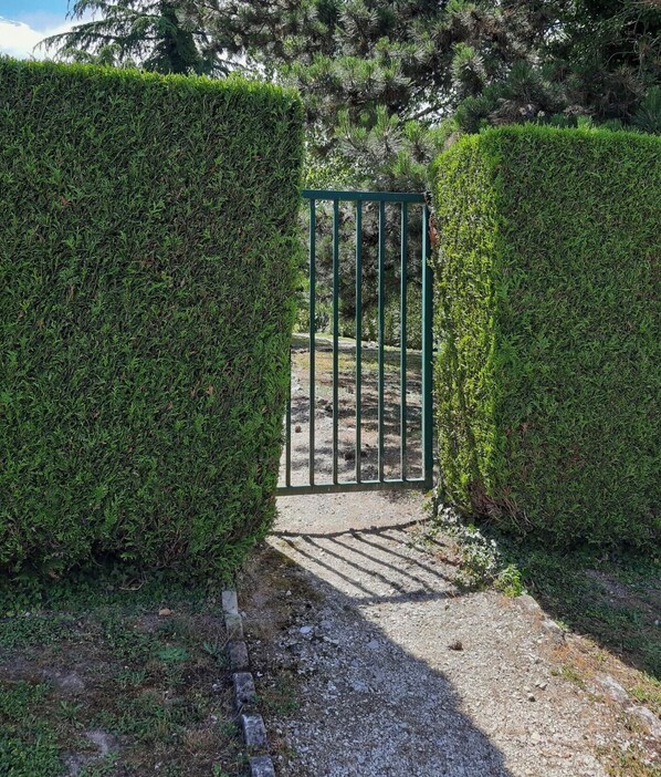 Une entrée fermée par un portail, avec un chemin de gravier qui traverse un arbuste taillé avec soin.