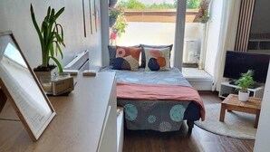 Un dormitorio moderno con cama, mesita de noche, televisor y vistas al exterior.