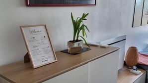 Un mostrador de recepción con un cartel de bienvenida enmarcado, una planta en maceta y una obra de arte colgada arriba.