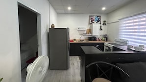 A compact kitchen with a refrigerator, microwave, stove, and a fan. - The Cosy Konak (Port of Spain)