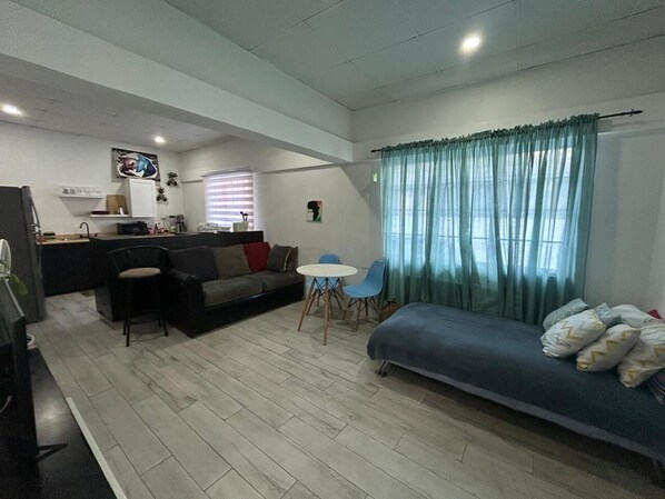A compact living space with a sofa, a small dining table, and a kitchenette. - The Cosy Konak (Port of Spain)