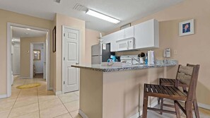 A compact kitchen with white cabinets, a granite countertop, and a wooden bar stool.