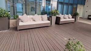 Eine moderne Außenbereich-Sitzgruppe mit zwei Sofas und Pflanzenkübeln vor einem großen Glasgebäude.