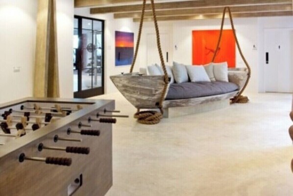 Ein modernes Wohnzimmer mit Kicker, einer Hängesitzschaukel und einer Couch mit Kissen.