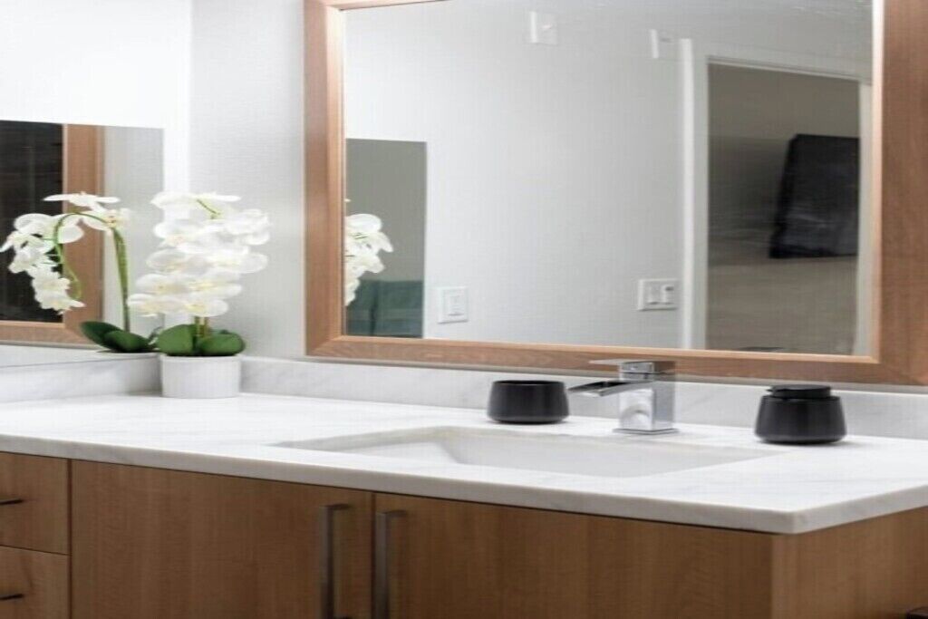 Une salle de bain moderne avec un grand miroir, deux vasques et une orchidée en pot.
