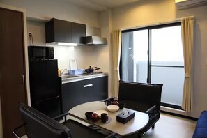A compact kitchen with a refrigerator, microwave, and a small countertop. There is a dining table with chairs, and a large window with curtains. - Enjoy exploring Okinawa Just a short walk from K / Naha City Okinawa (Naha City)