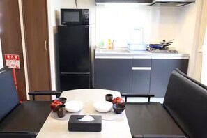 Eine kompakte Küche mit Mikrowelle, Kühlschrank und einer kleinen Spüle. Ein Esstisch mit Stühlen und einer Taschentuchbox steht daneben.