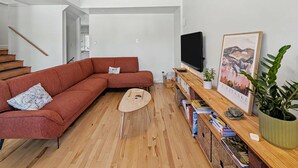Un salon moderne comprenant un canapé d’angle, un téléviseur à écran plat, une table basse en bois et une bibliothèque remplie de livres et d’objets décoratifs.