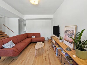 A modern living room with a sectional sofa, a flat-screen TV, a wooden coffee table, and a bookshelf with books and decorative items.