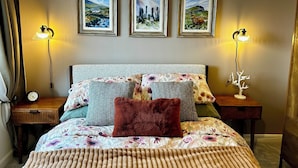 A bedroom with a bed, two bedside tables, a wall clock, and three framed pictures.