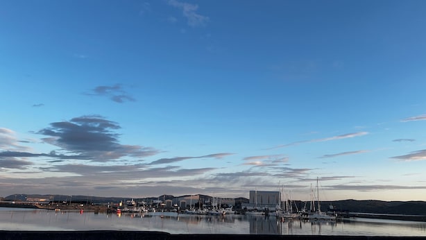 A marina with boats docked, a building with a flat roof, and a calm water body reflecting the sky.