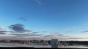 Ein Yachthafen mit vertäuten Booten, ein Gebäude mit flachem Dach und ruhigem Gewässer, das den Himmel spiegelt.