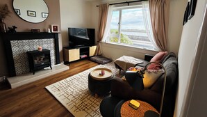A living room with a fireplace, a television, a sofa, and a window with curtains.