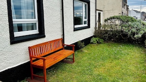 A wooden bench outside a building with white walls and black window frames.