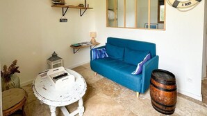 Een woonkamer met een blauwe bank, een ronde salontafel, een houten vat, een spiegel en een decoratieve reddingsboei.