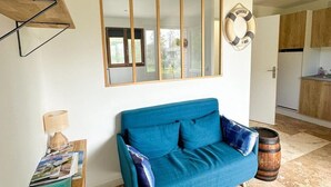 Een woonkamer met een blauwe bank, een houten salontafel, een lamp, een tijdschriftrek, een decoratieve reddingsboei en een vat.