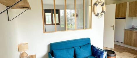 Una sala de estar con un sofá azul, una mesa de centro de madera, una lámpara, un atril para revistas, un adorno con un flotador de salvavidas y un barril.
