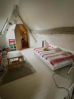 Een kleine slaapkamer in zolderstijl met een enkel bed, een houten tafel en een stoel.