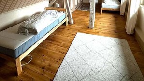 Ein kleines Schlafzimmer im Dachgeschoss mit schrägen Wänden, zwei hölzernen Betten, einem großen Fenster und einem Holzboden.