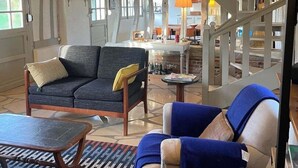 Ein geräumiger Wohnbereich mit hohen Decken, freiliegenden Holzbalken, einem Sofa, einem Sessel und einem kleinen Tisch.