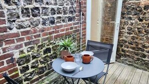 Eine Terrasse mit Tisch, Stühlen, einem Blumentopf und einer Tür zu einem Innenraum.