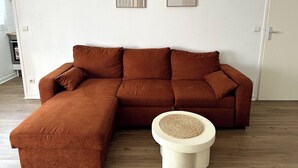 Um sofá modular marrom com um banquinho combinando, um banquinho pequeno trançado e duas obras de arte abstratas nas paredes.