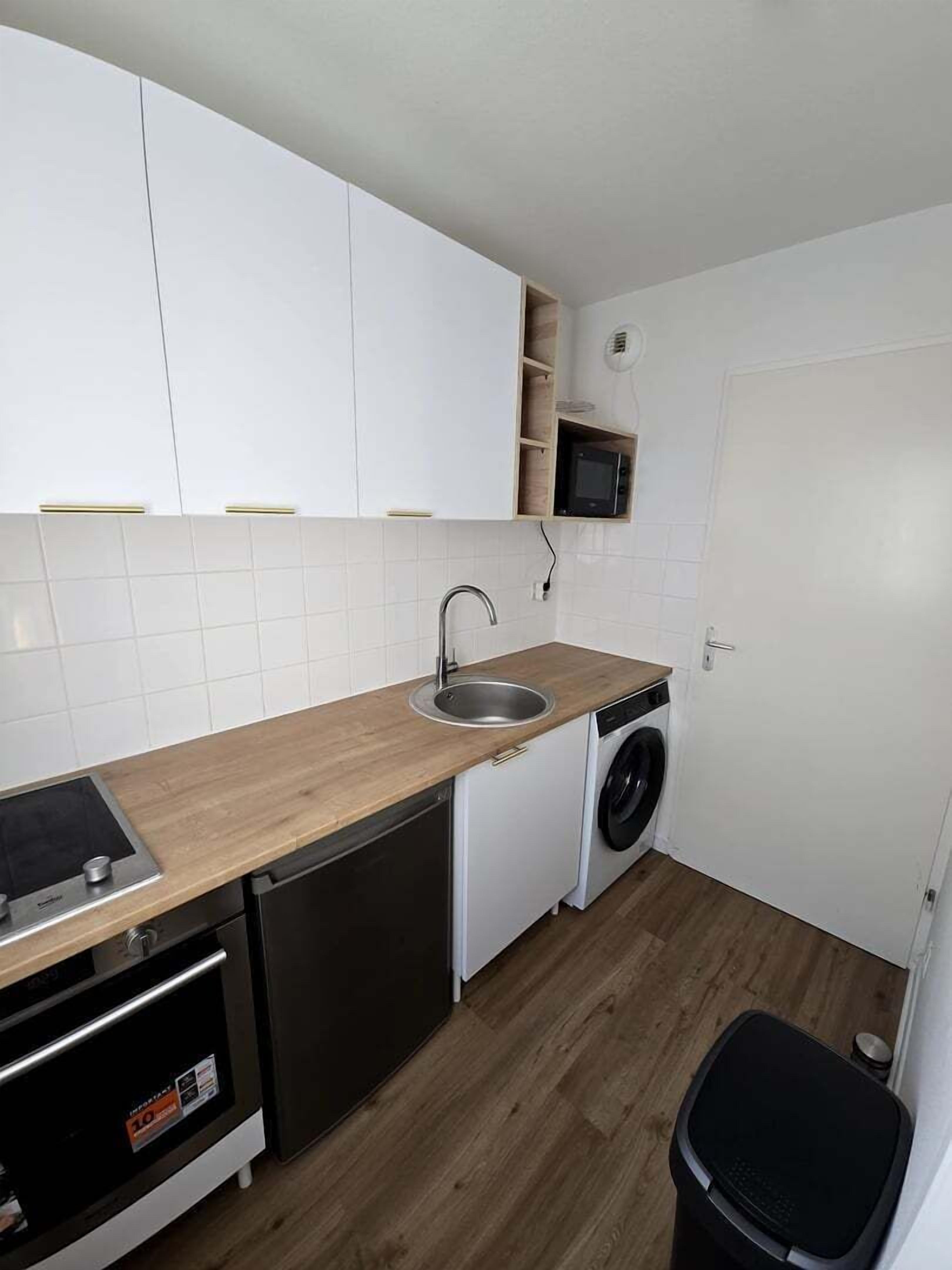 A compact kitchen with white cabinets, a sink, a microwave, a dishwasher, and a washing machine.