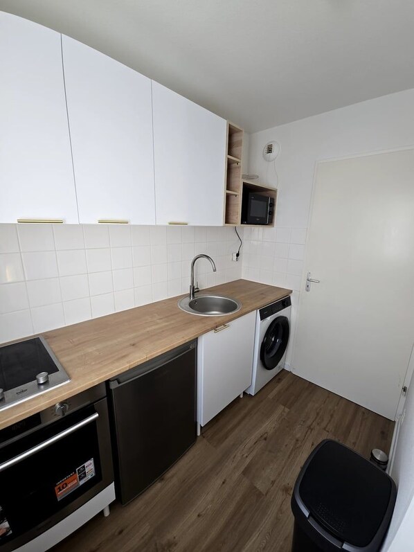 A compact kitchen with white cabinets, a sink, a microwave, a dishwasher, and a washing machine.