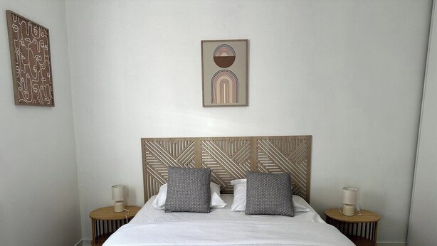 Cama bem arrumada com duas almofadas, cabeceira de madeira e duas mesas de cabeceira com abajures.