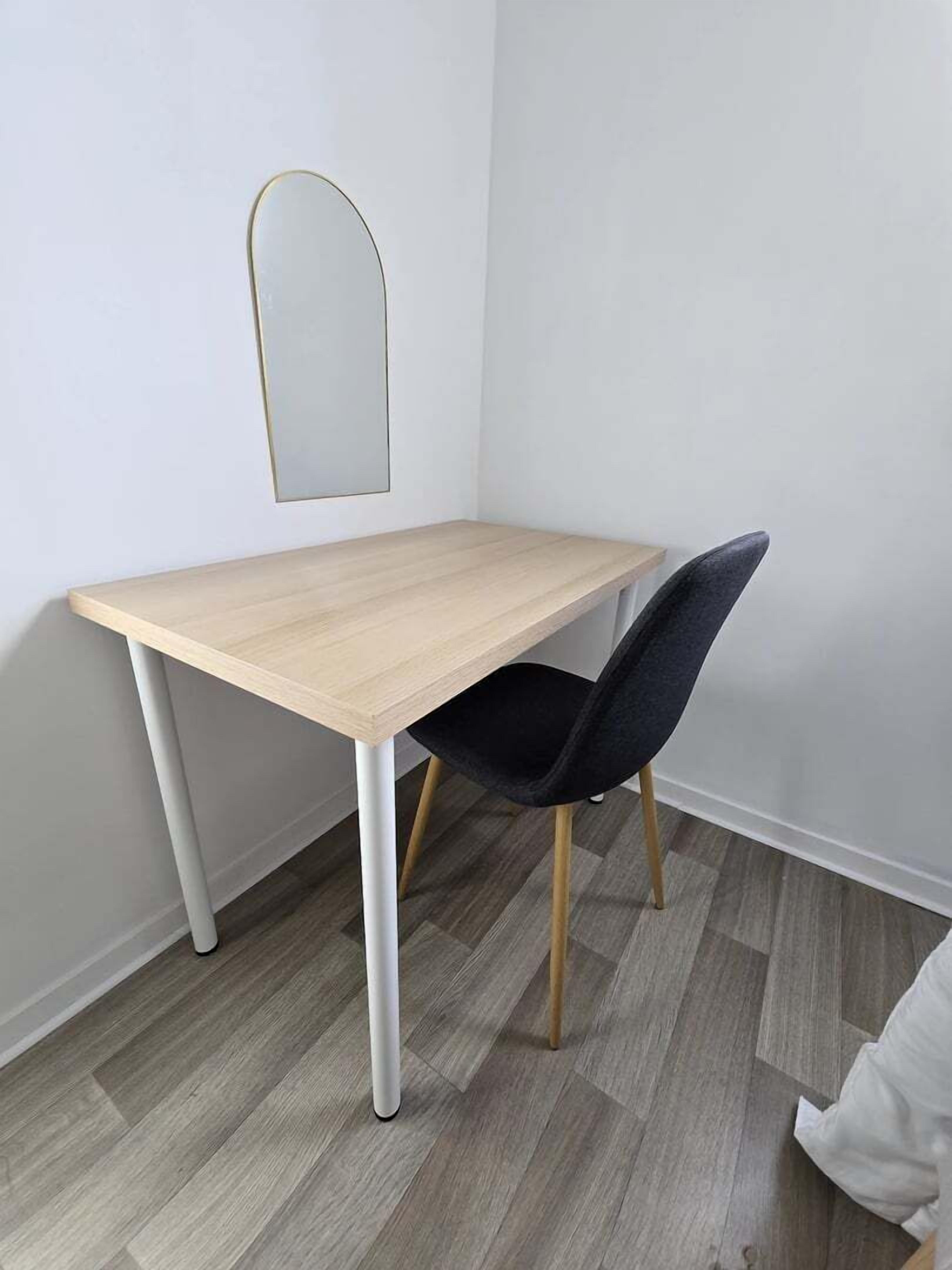 Une petite pièce moderne, dotée d’un bureau en bois clair et d’une chaise foncée.