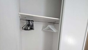 Um closet amplo com piso de madeira, porta branca e uma barra de metal com cabides.