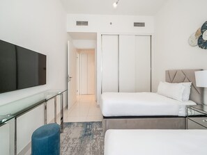 A modern hotel room with a large flat-screen TV, a bed with a headboard, a bedside table, and a wardrobe with sliding doors. - Beachfront Living With Marina Skyline Views (Dubai)