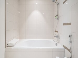 A modern bathroom with a white bathtub, a shower area, and a towel rack. - Beachfront Living With Marina Skyline Views (Dubai)
